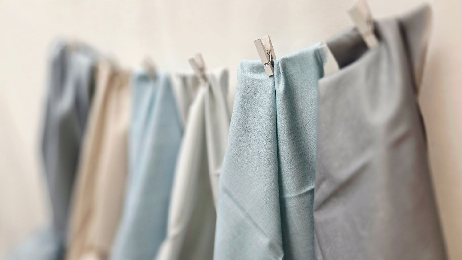 Pastel fabric swatches in blue and beige tones hanging on a clothesline with wooden pegs.