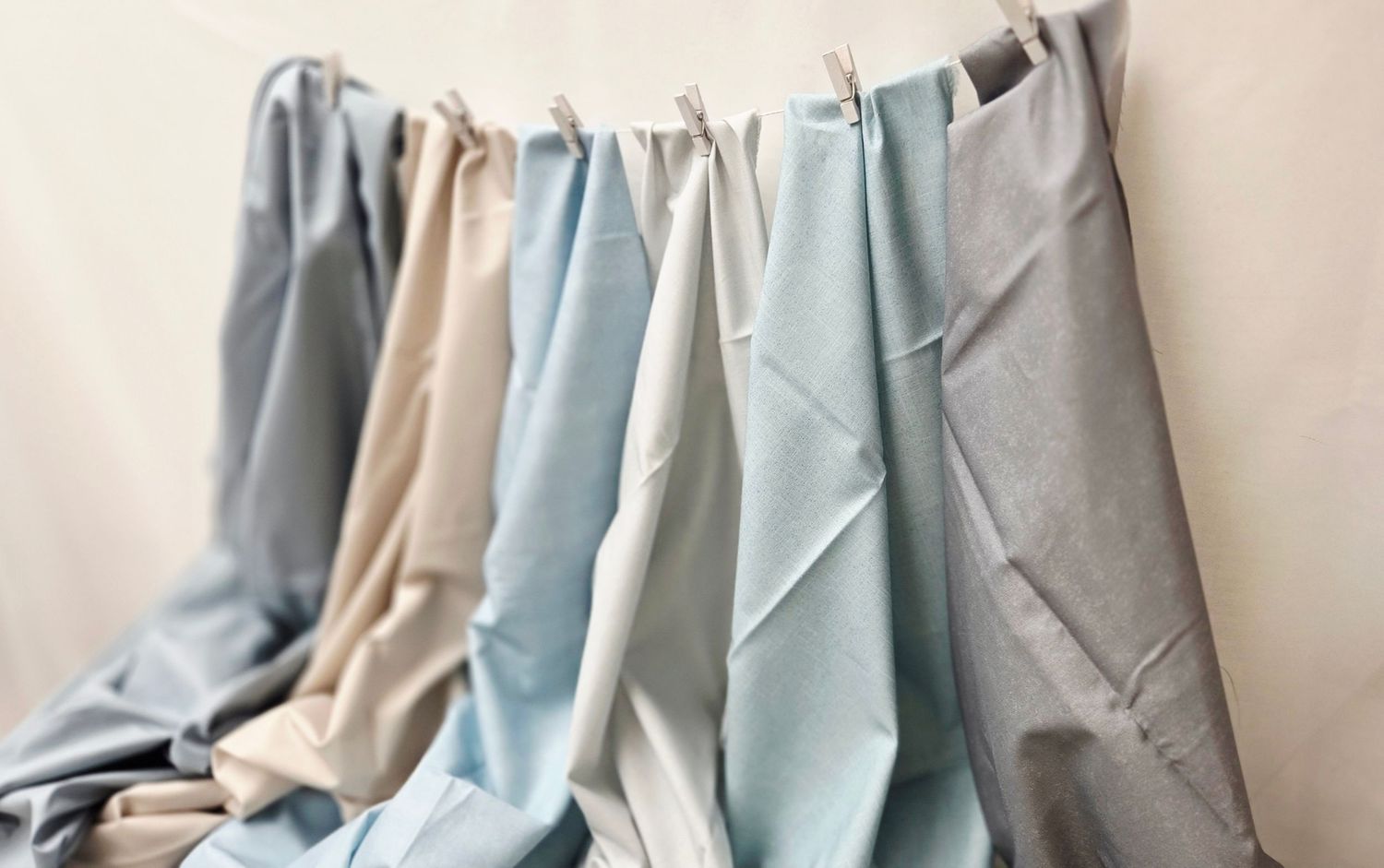 Soft fabric swatches in neutral and pastel tones hang draped on a rod, showcasing linen textile colors.