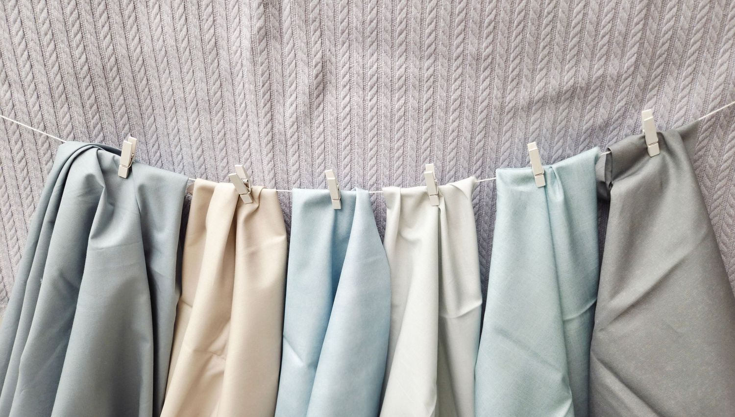 Colorful pastel fabric swatches hanging on a clothesline with wooden pegs against a striped background.