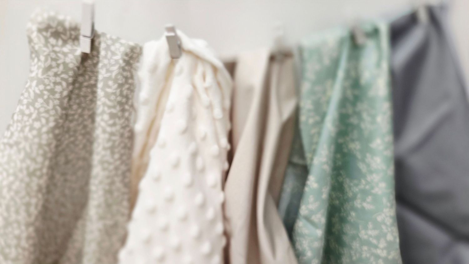 Assorted pastel fabric swatches hanging on a rack, including floral prints and textured minky cloth.