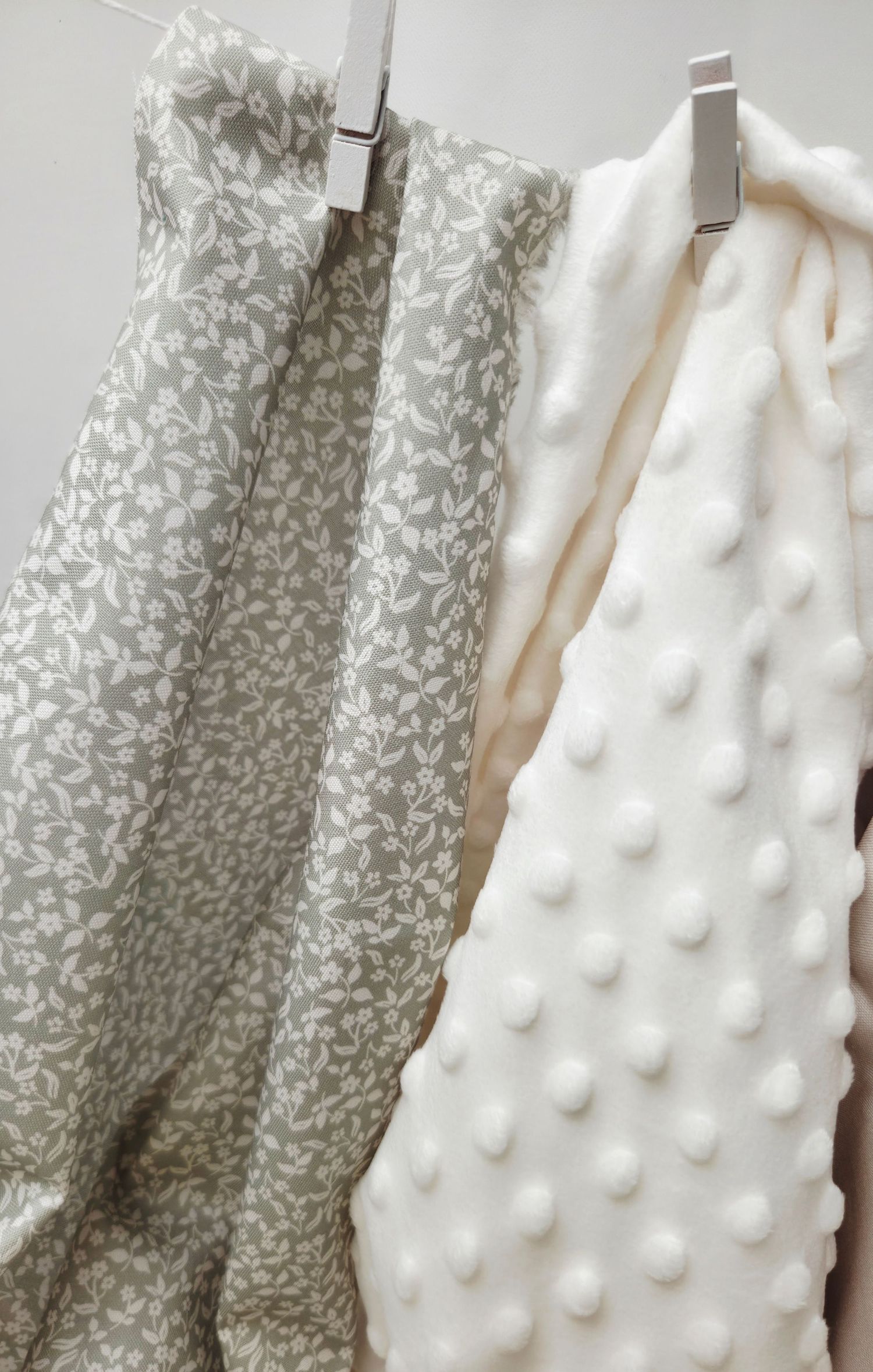 Two baby blankets hanging on clips, one gray floral cotton and one cream minky dot fabric.