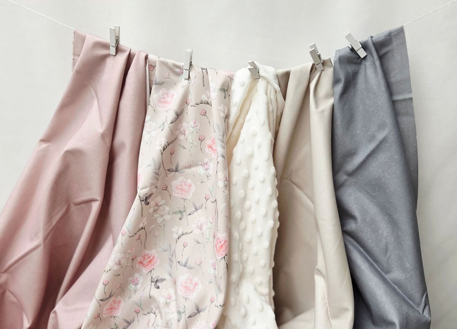 Four fabric swatches in pink, floral, cream, tan, and gray hang from clips on a white rod.