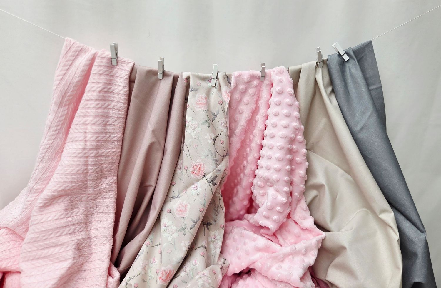 Soft pink, beige, and gray baby blankets hanging on a clothesline, showcasing various textures and patterns.