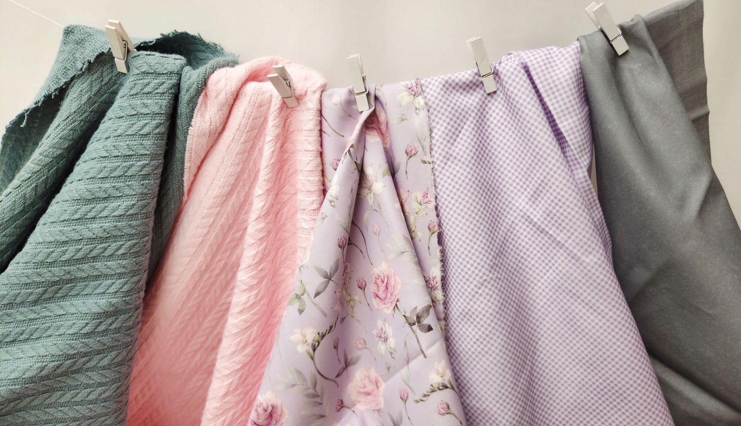 Colorful fabric swatches in pink, floral, lavender, and gray hanging on a clothesline with wooden clips.
