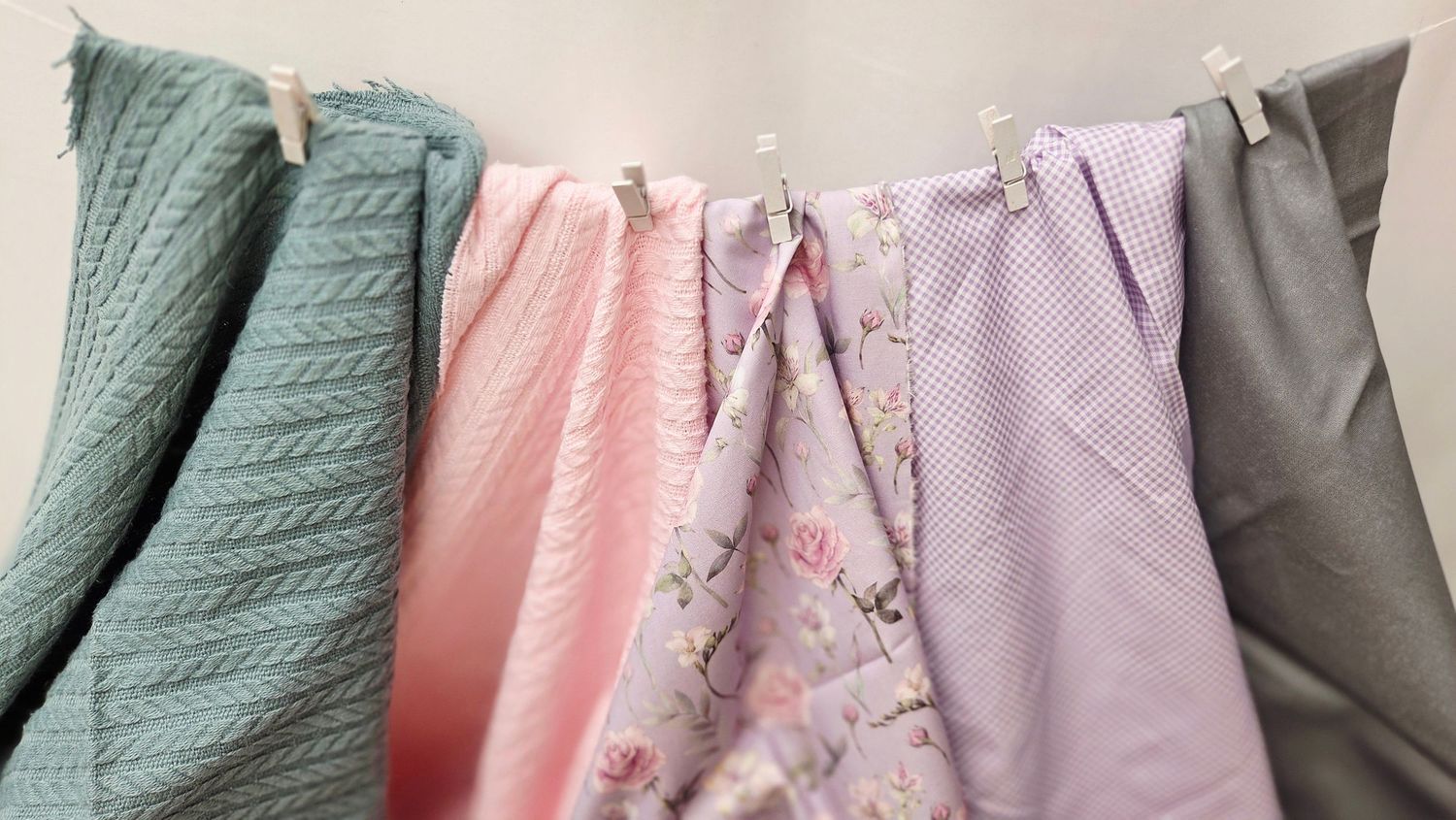 Colorful fabric swatches in pink, green, floral, and gray hanging on a clothesline with white clips.