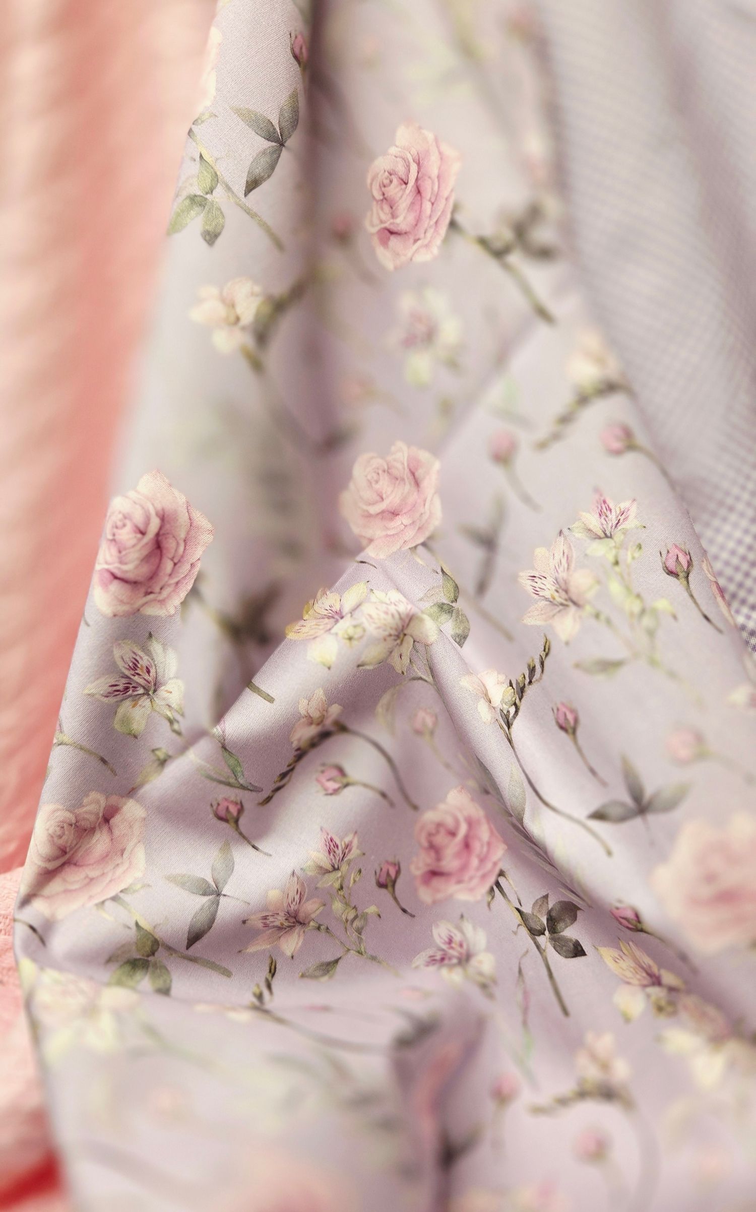 Soft lavender fabric with delicate pink rose floral print pattern, draped elegantly with gentle folds and blurred pink background.