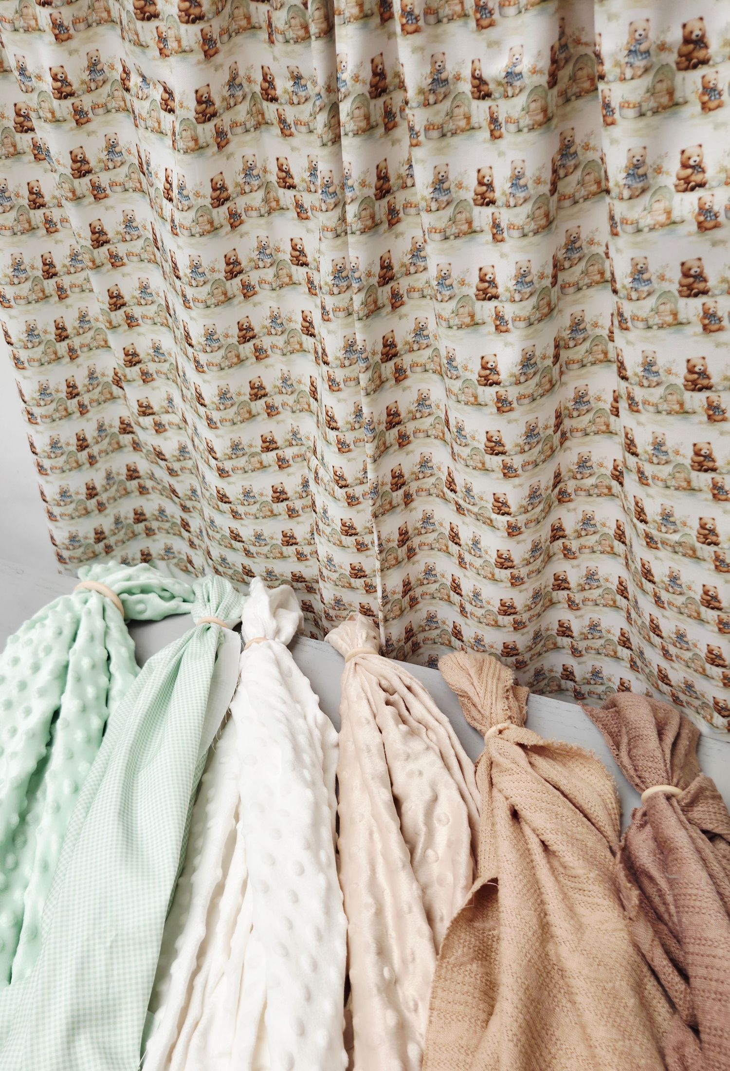 Assorted baby blankets in mint, white, and peach tones displayed against a teddy bear print curtain backdrop.