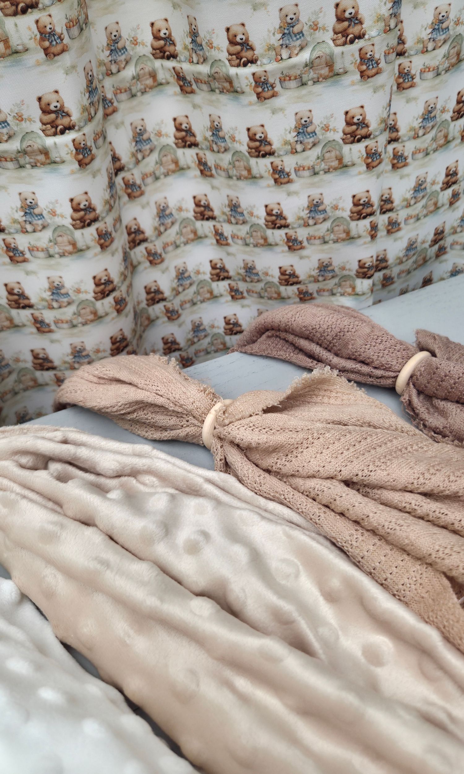 Baby crib bumper with teddy bear print alongside soft pink knitted blanket and plush minky fabric.