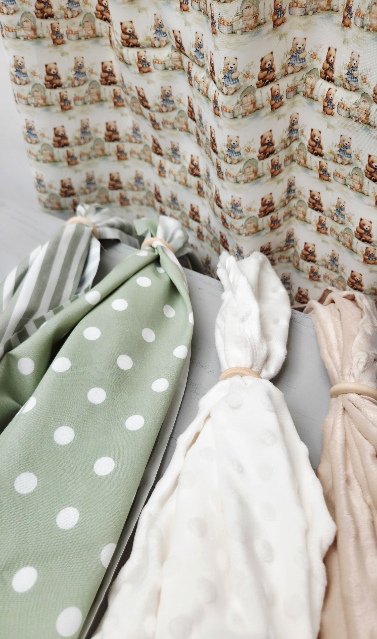 Assorted baby fabrics including green polka dot, white minky, beige muslin, and teddy bear print nursery textiles.