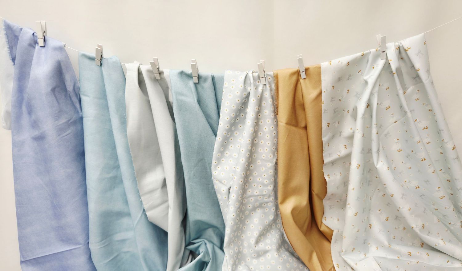 Colorful fabric swatches hanging on a clothesline, including blue, white, floral, and tan textiles.