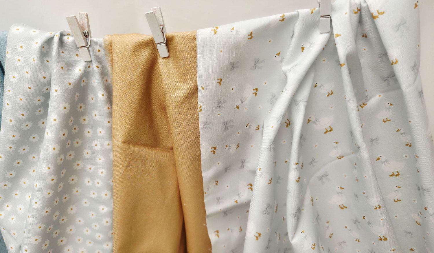 Four fabric swatches in yellow and white with floral patterns hanging on a clothesline with wooden pegs.