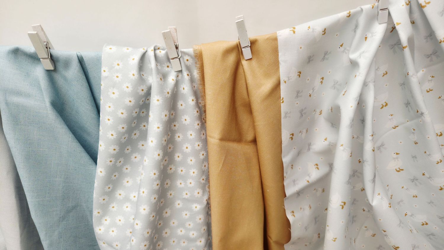 Colorful fabric swatches in blue, white, and yellow hanging on a clothesline with wooden pegs.