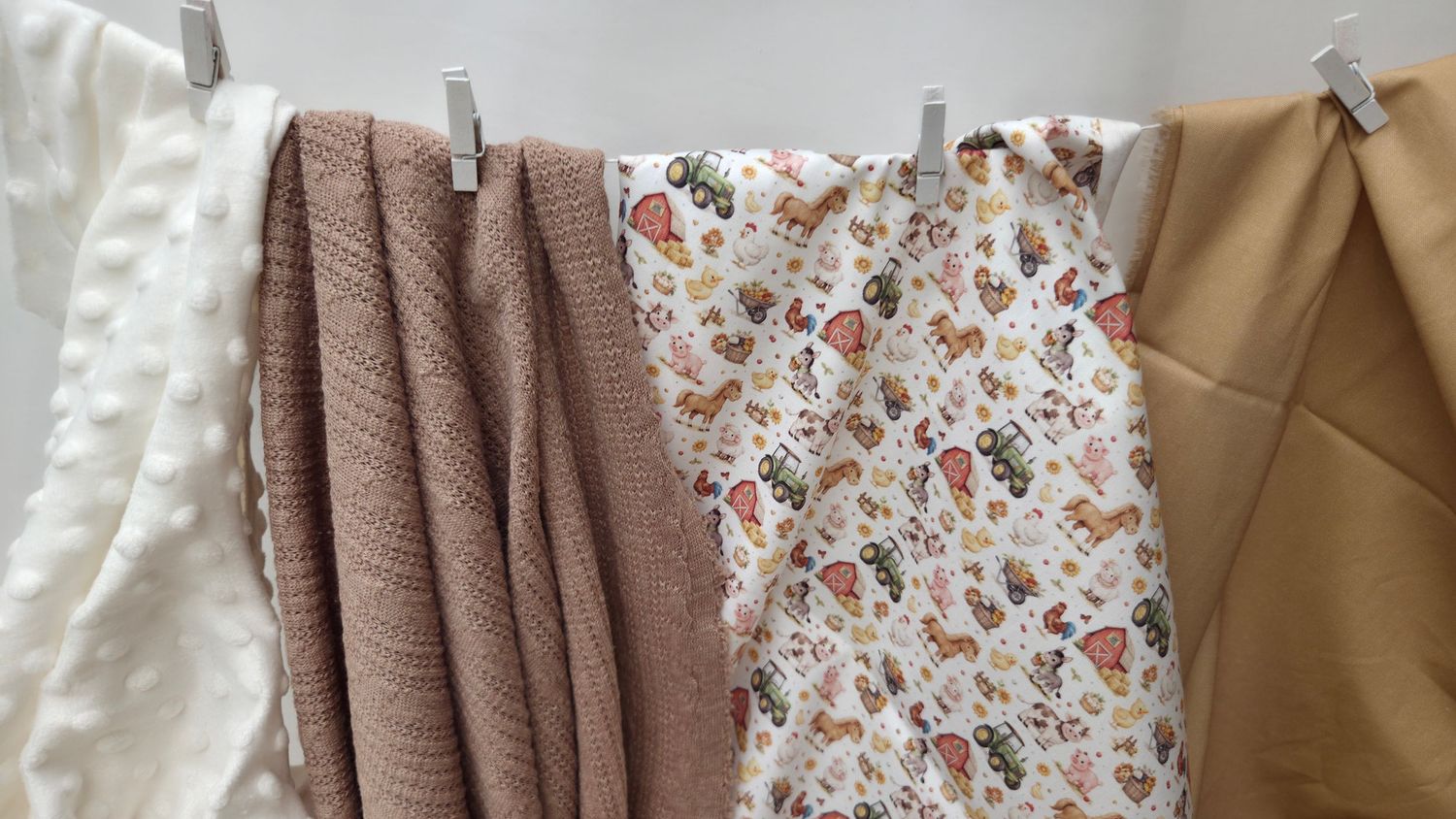 Four fabric swatches hang on a line, featuring white, mauve knit, floral print, and tan solid textiles.