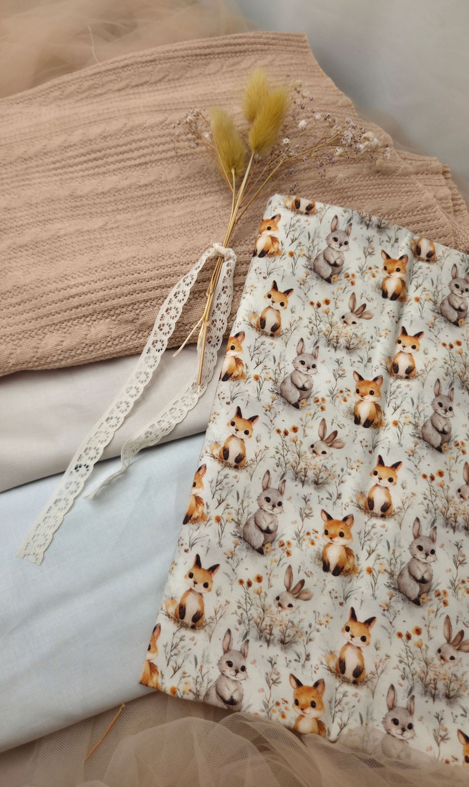 Handmade fabric pouch with woodland fox and bunny print, lace ribbon tie, displayed with knit blanket and dried flowers.