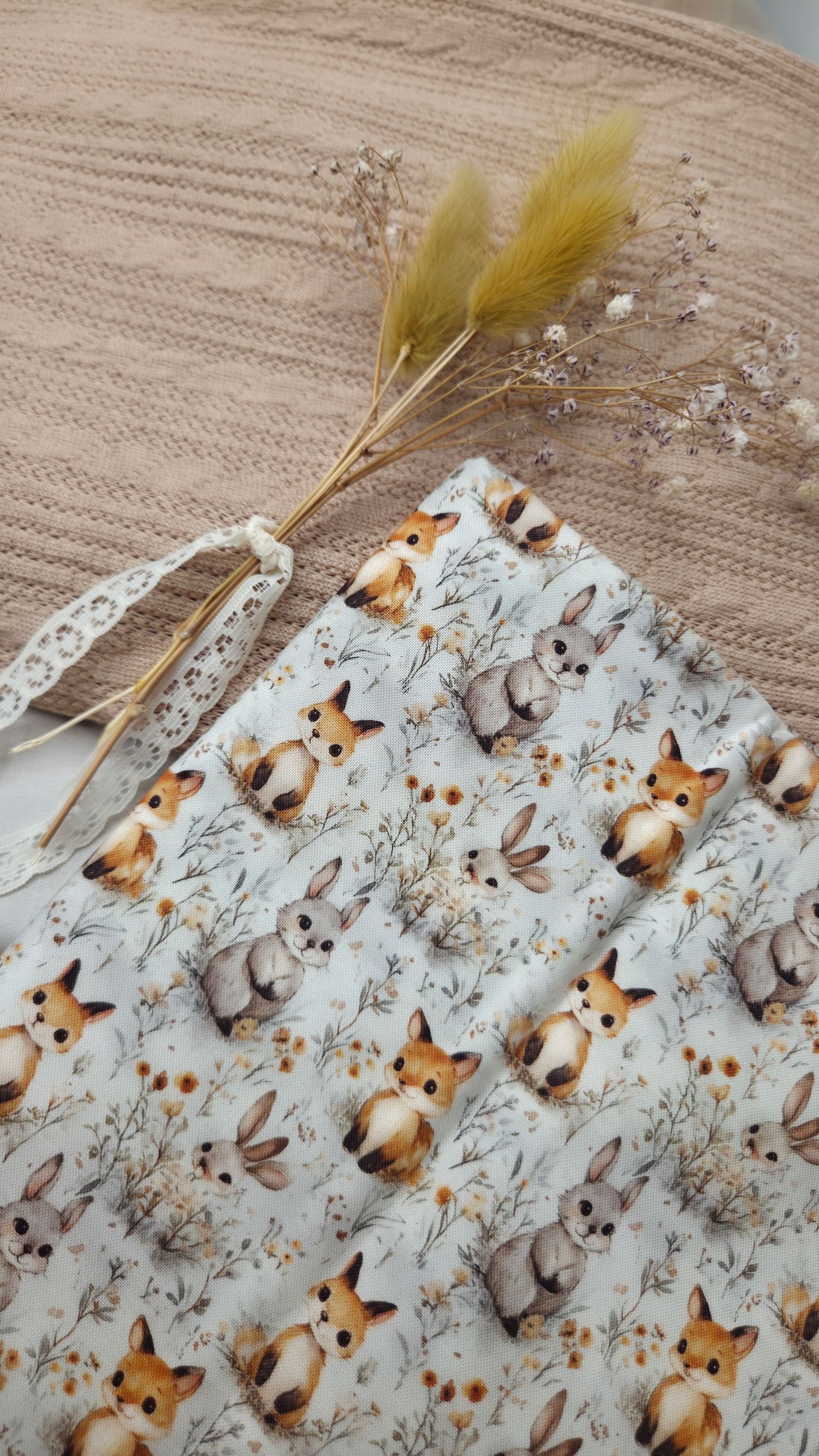 Cute woodland animals fabric featuring foxes and bunnies with floral accents, displayed with dried flowers on a woven surface.