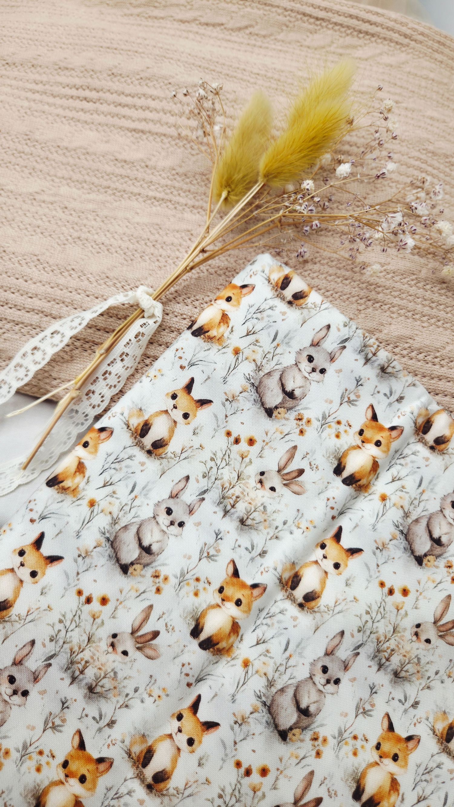Cute woodland animal print fabric featuring foxes and bunnies with floral details, displayed with dried flowers.