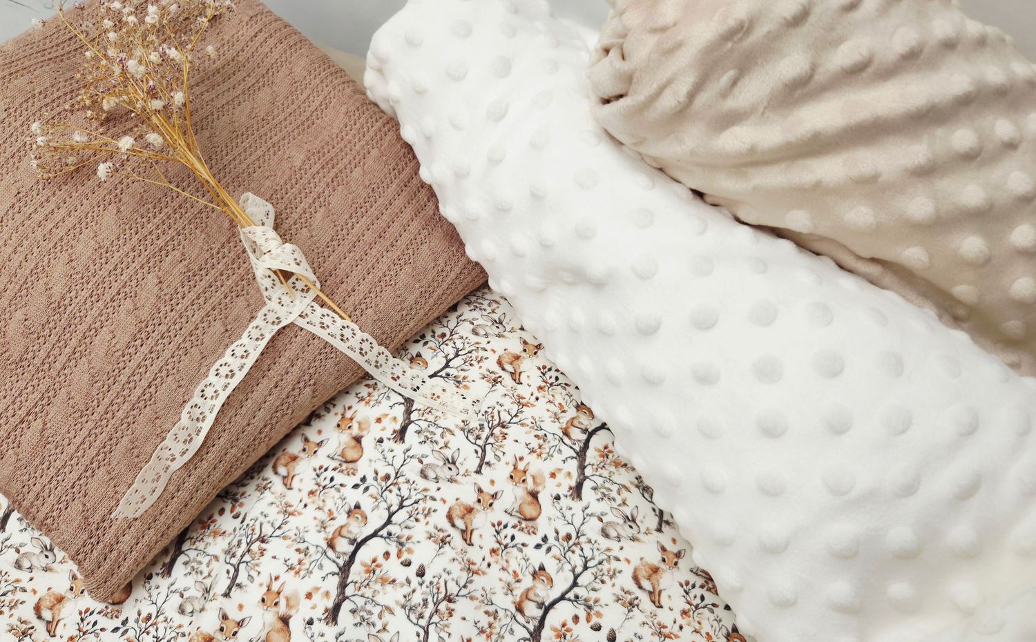 Cozy neutral-toned baby bedding set featuring floral fabric, knit blanket with lace trim, and textured minky dot pillow.