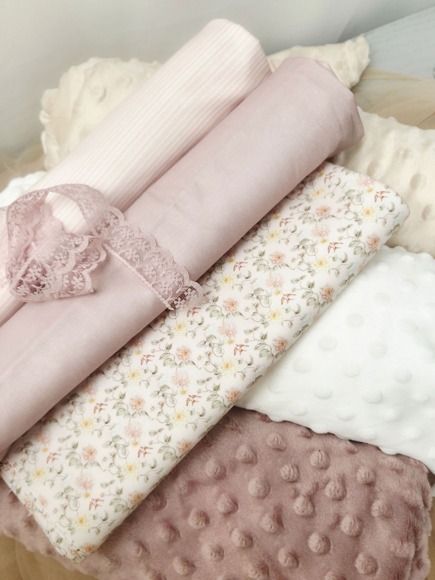 Soft pink baby blankets with floral print, ribbed fabric, lace trim, and textured minky dot material arranged together.