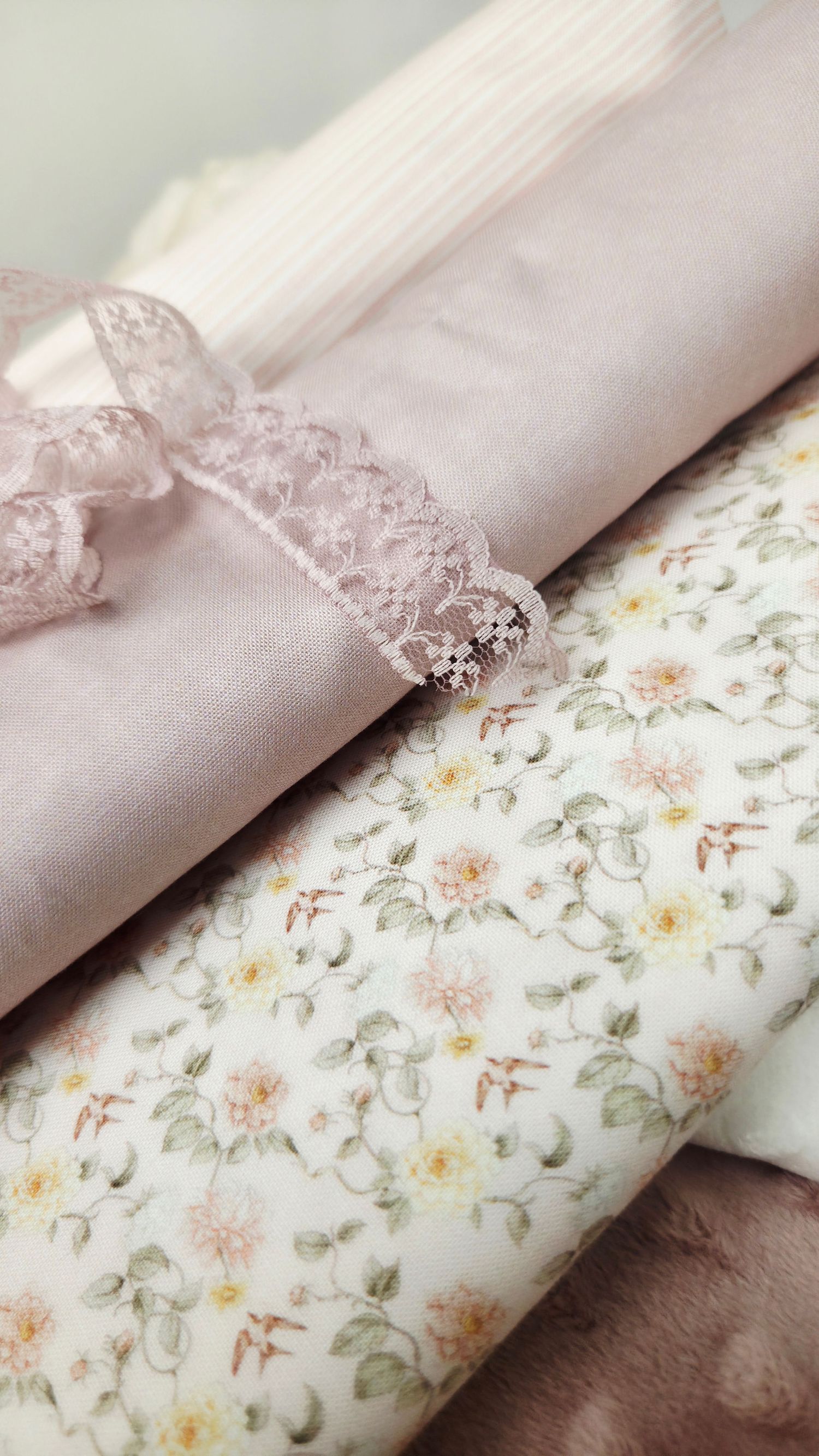 Folded pink fabric with delicate lace ribbon bow and floral print textile, soft pastel tones for sewing or crafting projects.