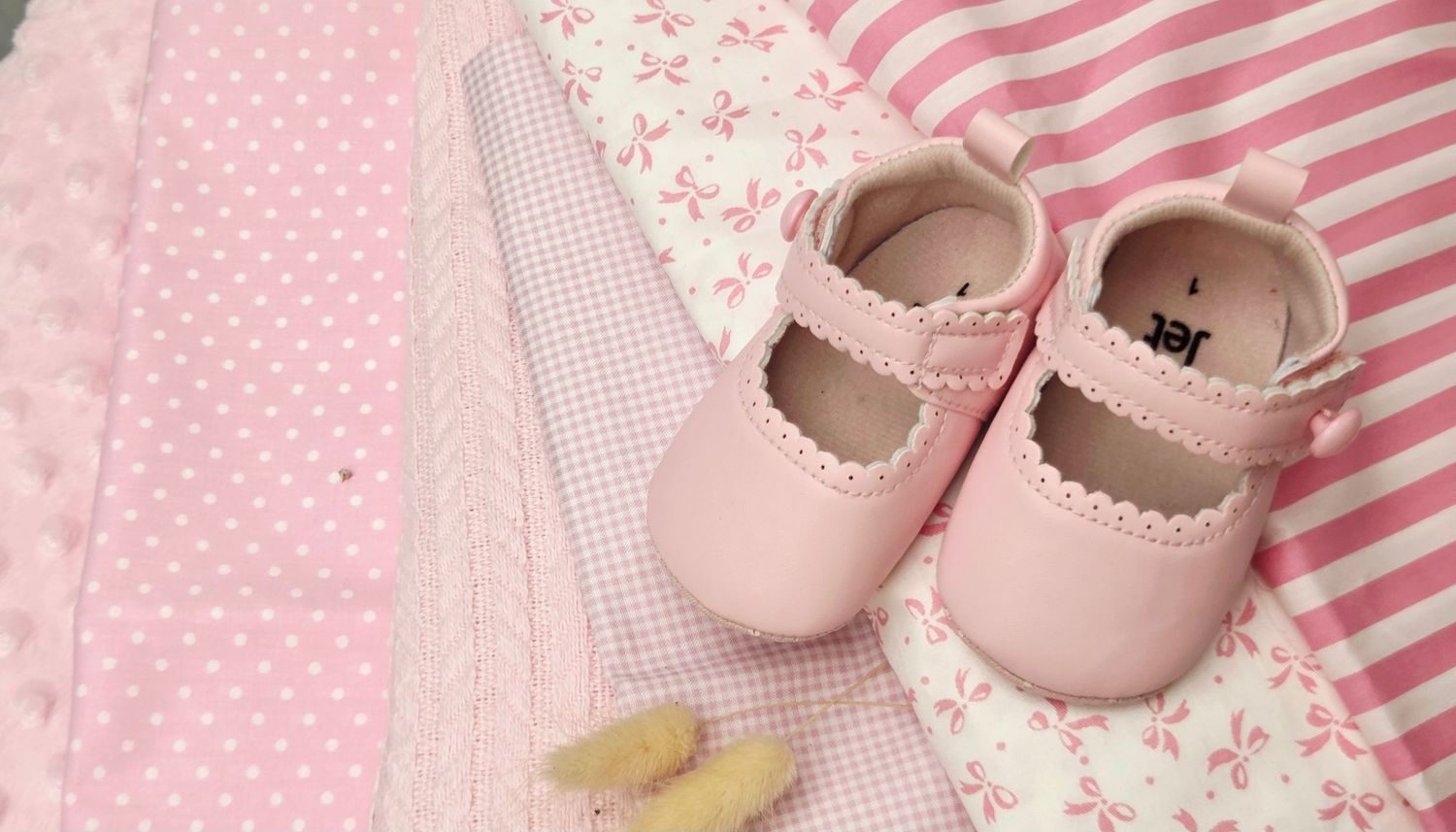 Pink baby girl shoes resting on soft pink fabric with floral and polka dot patterns, perfect for newborn gifts.