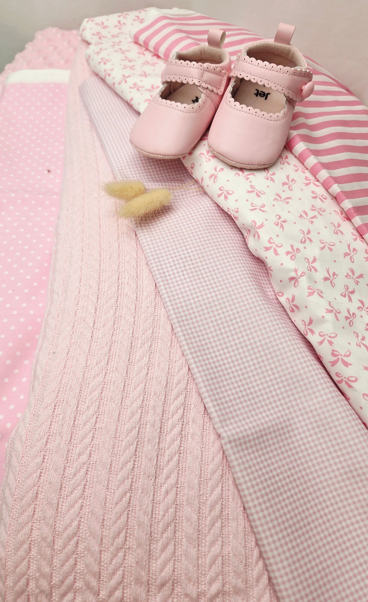 Pink baby girl flat lay with Mary Jane shoes, quilted blanket, gingham and floral fabrics, and polka dot textiles.