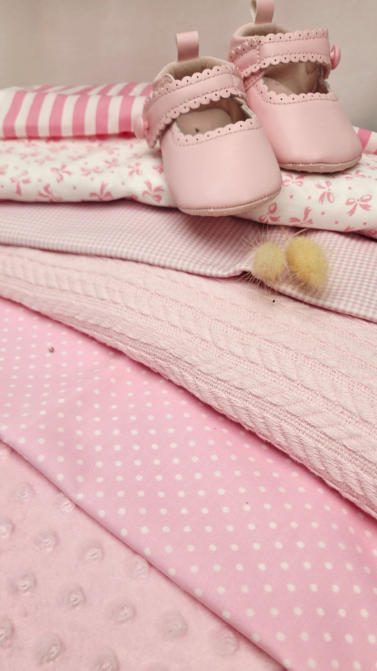 Pink baby girl items including soft blankets, patterned onesies, and delicate leather Mary Jane shoes neatly arranged together.