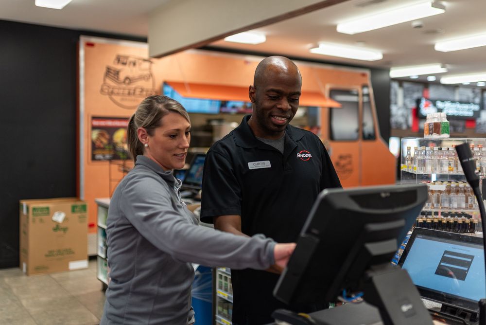 Two retail employees smiling while working together at a point-of-sale register in a store.