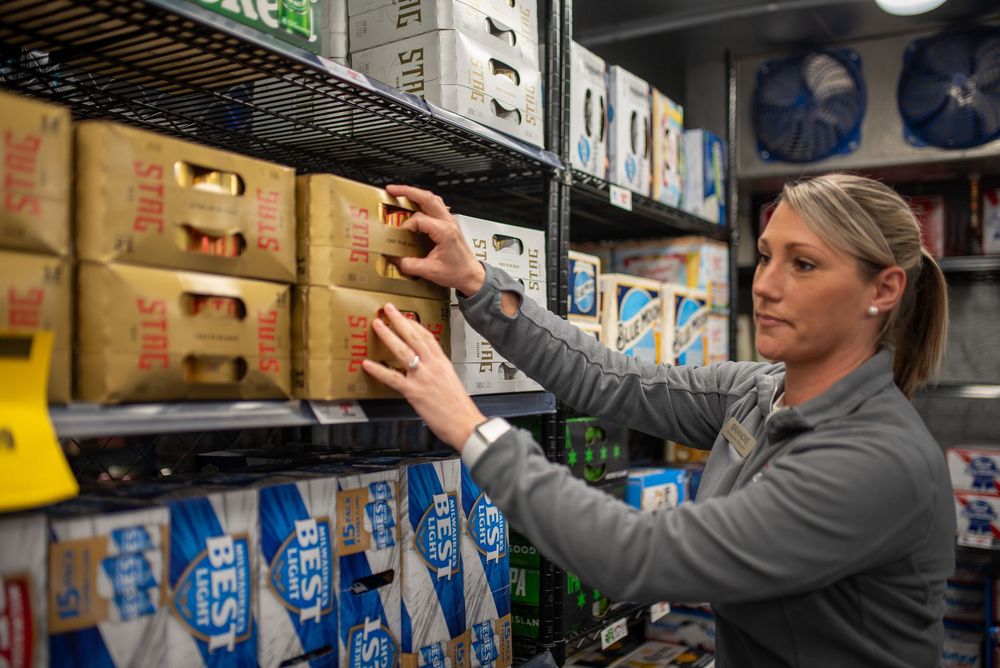 Woman stocking shelves with boxed beverages in a refrigerated storage room of a retail store.