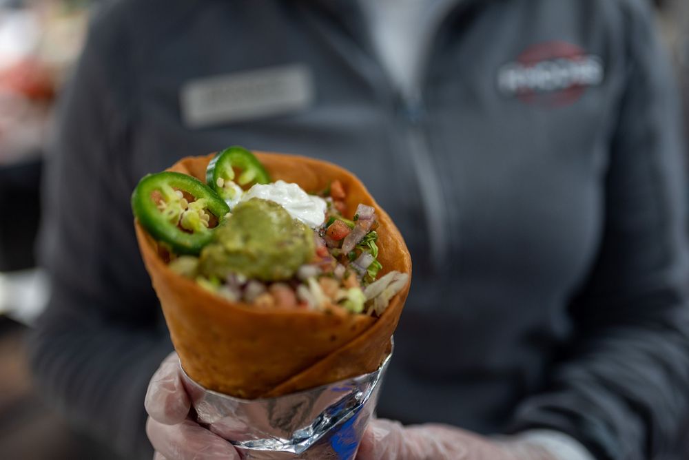 A hand holding a crispy tortilla cone filled with guacamole, sour cream, jalapeños, and fresh toppings.