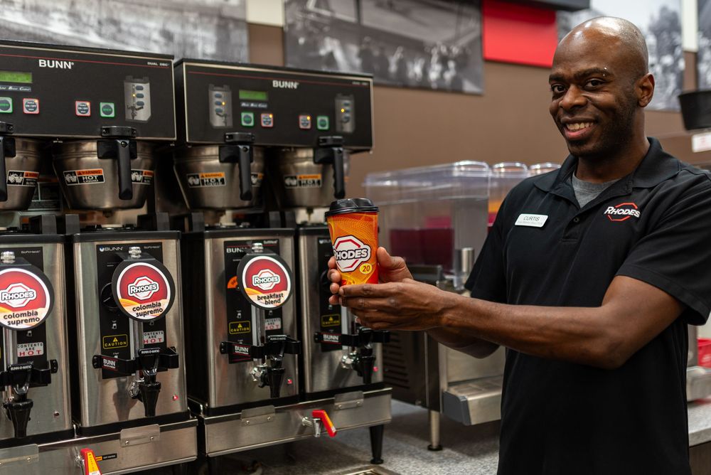 Smiling employee holding a coffee cup next to commercial Bunn coffee brewers in a restaurant.