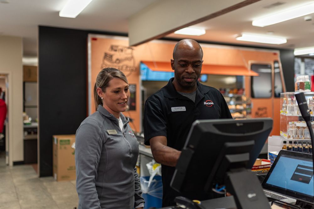 Two retail employees collaborate at a point-of-sale terminal in an auto parts store.