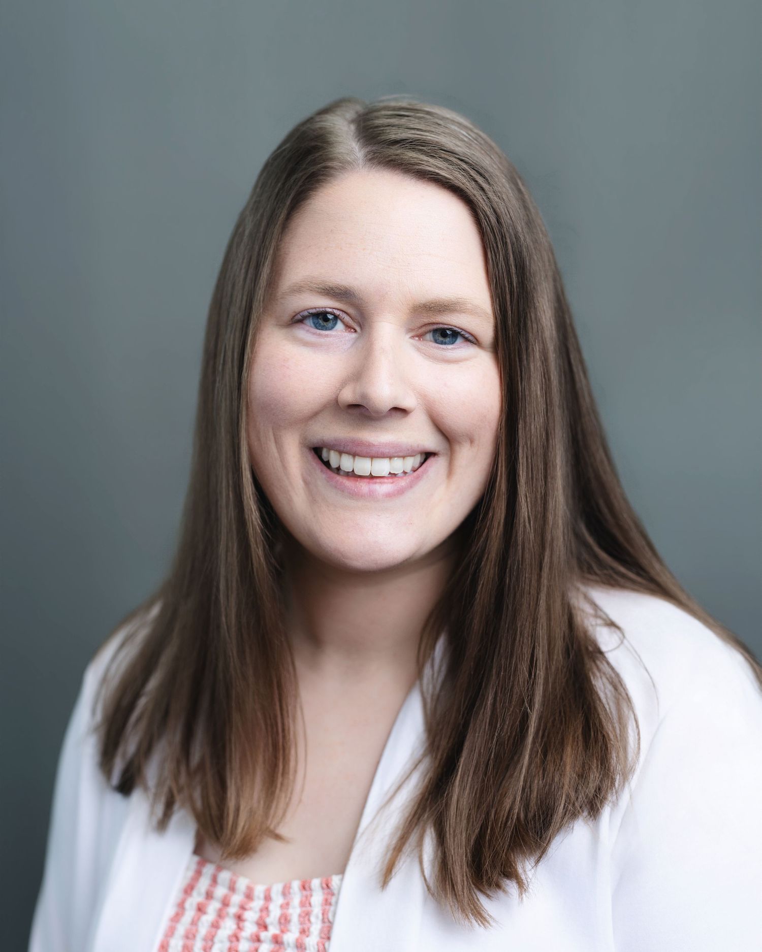 Smiling woman with long brown hair wearing a white coat in a professional headshot photo.