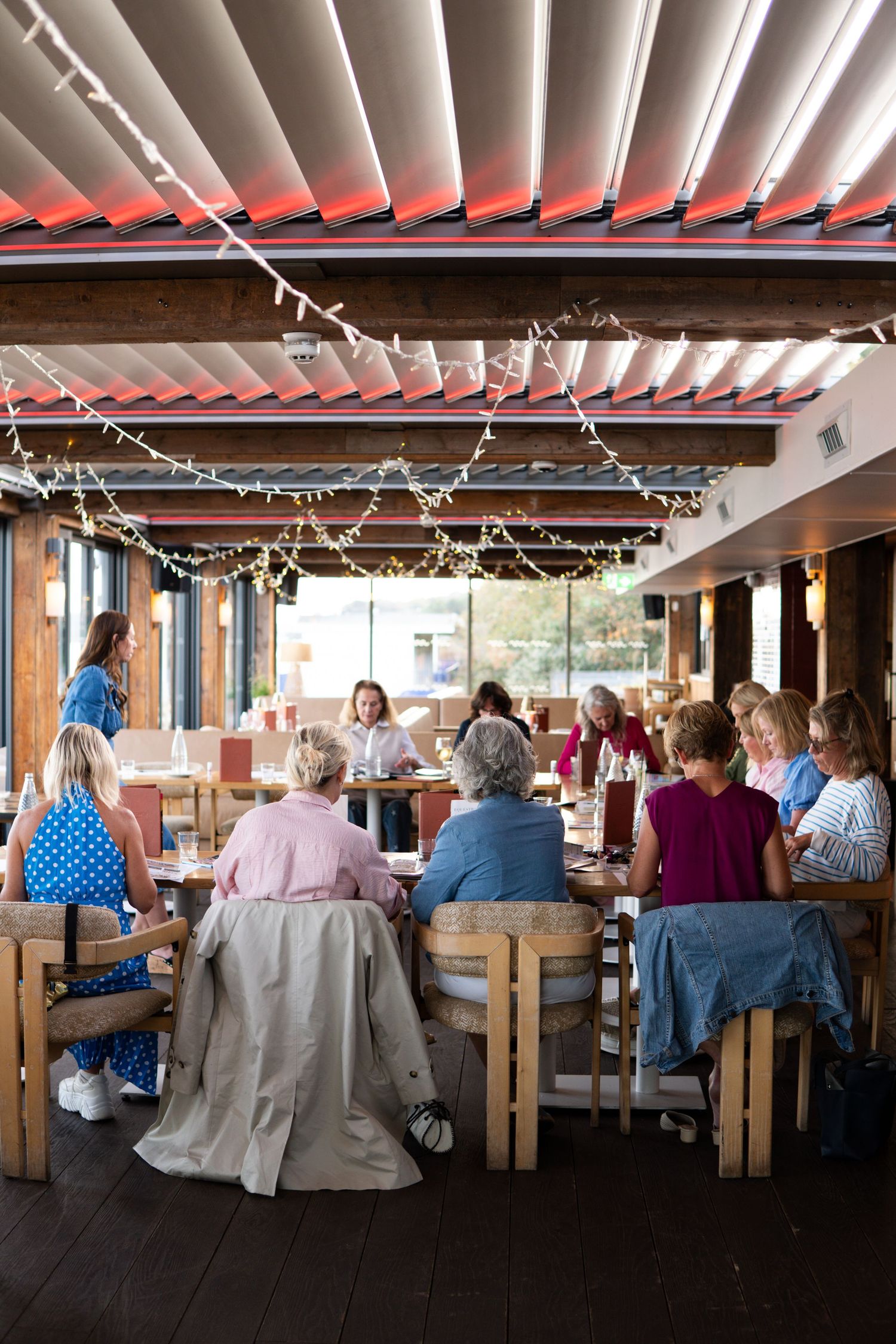 Women dining together at a sunny outdoor restaurant patio, enjoying wine and conversation in summer attire.