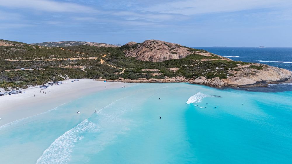 Aerial view of a stunning turquoise bay with white sandy beach, rocky headland, and clear blue waters in Australia.