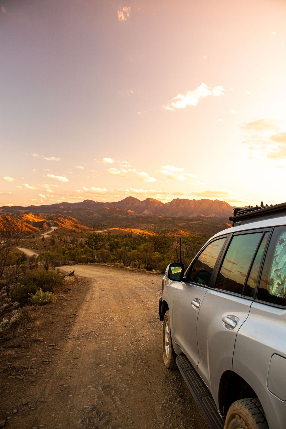 Silver SUV parked on a dirt road at sunset with dramatic mountain landscape and golden sky in the Australian outback.