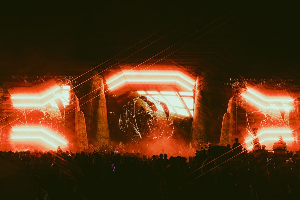 Spectacular stage light show with glowing red beams and silhouetted crowd at a music festival.