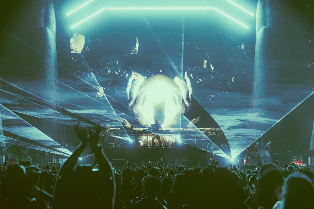 Concert crowd with blue laser light show and glowing stage display at music festival.