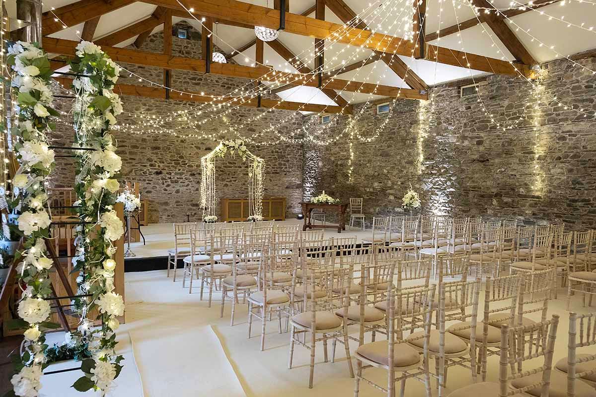 Elegant barn wedding venue at New House Farm with fairy lights, white floral arch, and rows of gold chiavari chairs set for a ceremony.