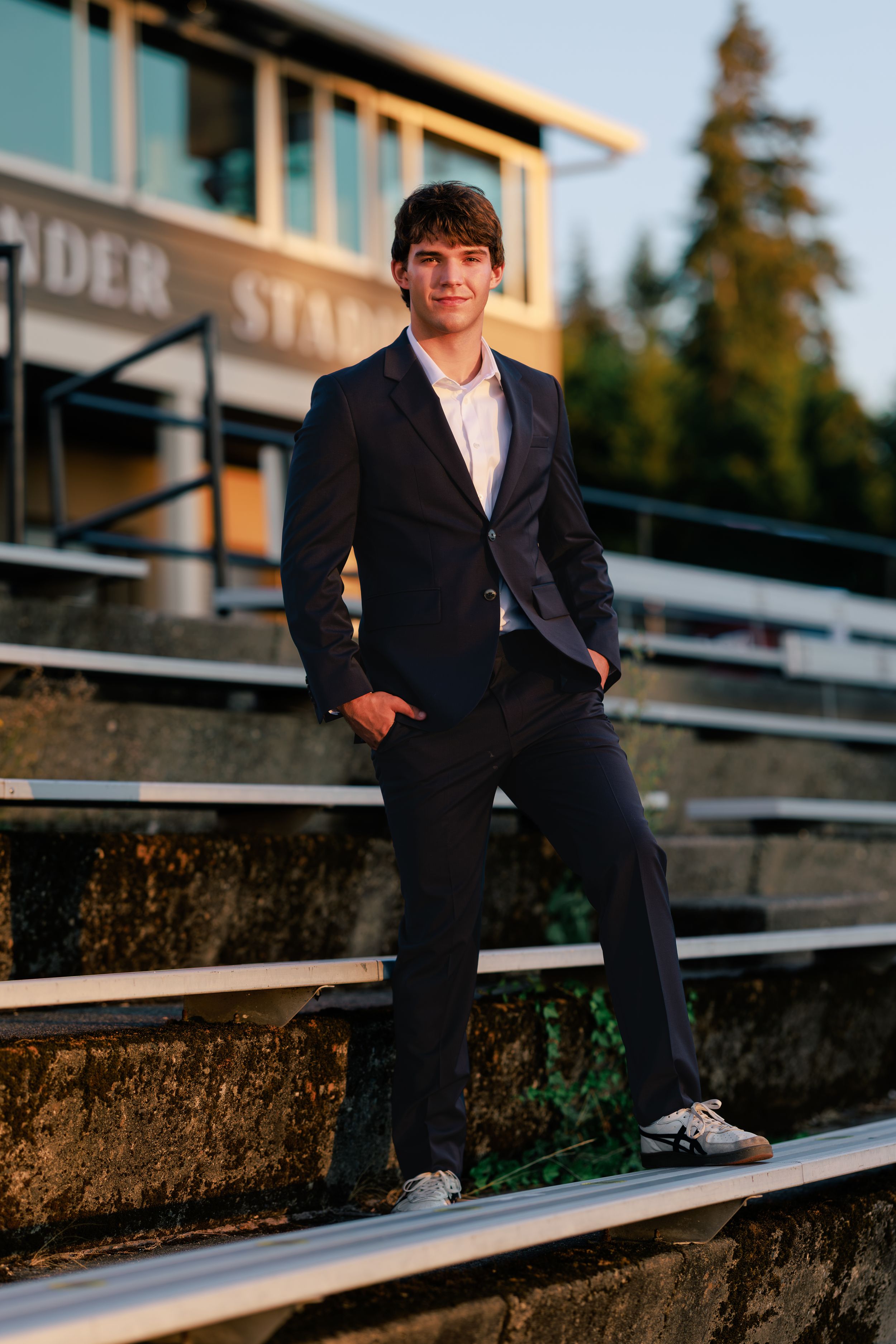 Young man in navy suit posing confidently on stadium bleachers during golden hour photography session.
