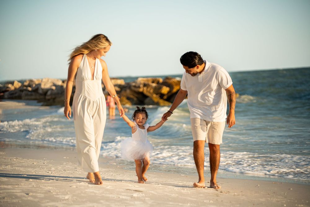 Family of three enjoying a sunny beach day, parents swinging their toddler daughter over the waves.