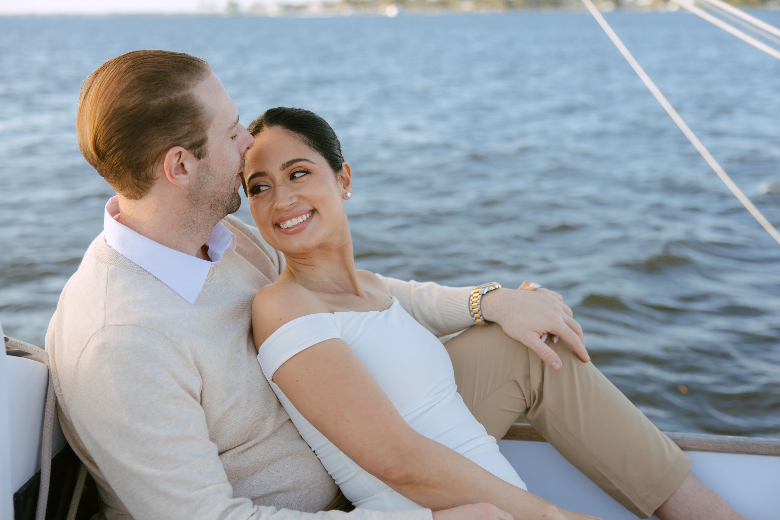 Couple sharing a tender moment on a sailboat, woman smiling as man kisses her cheek.