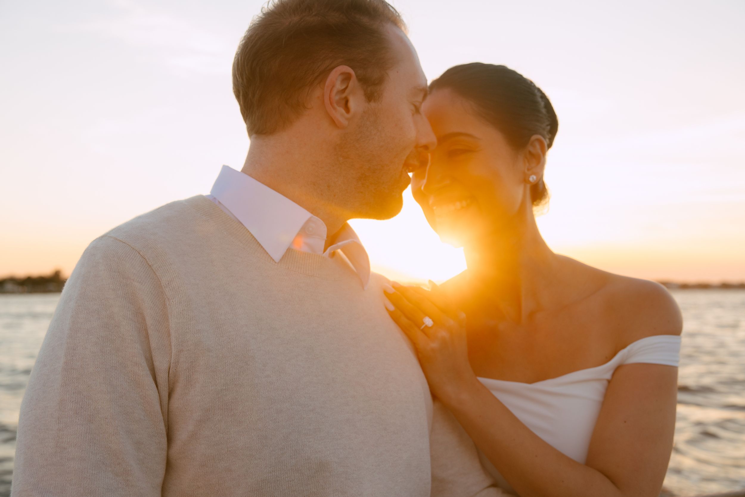 Couple sharing an intimate moment at sunset by the water, golden light glowing behind them.