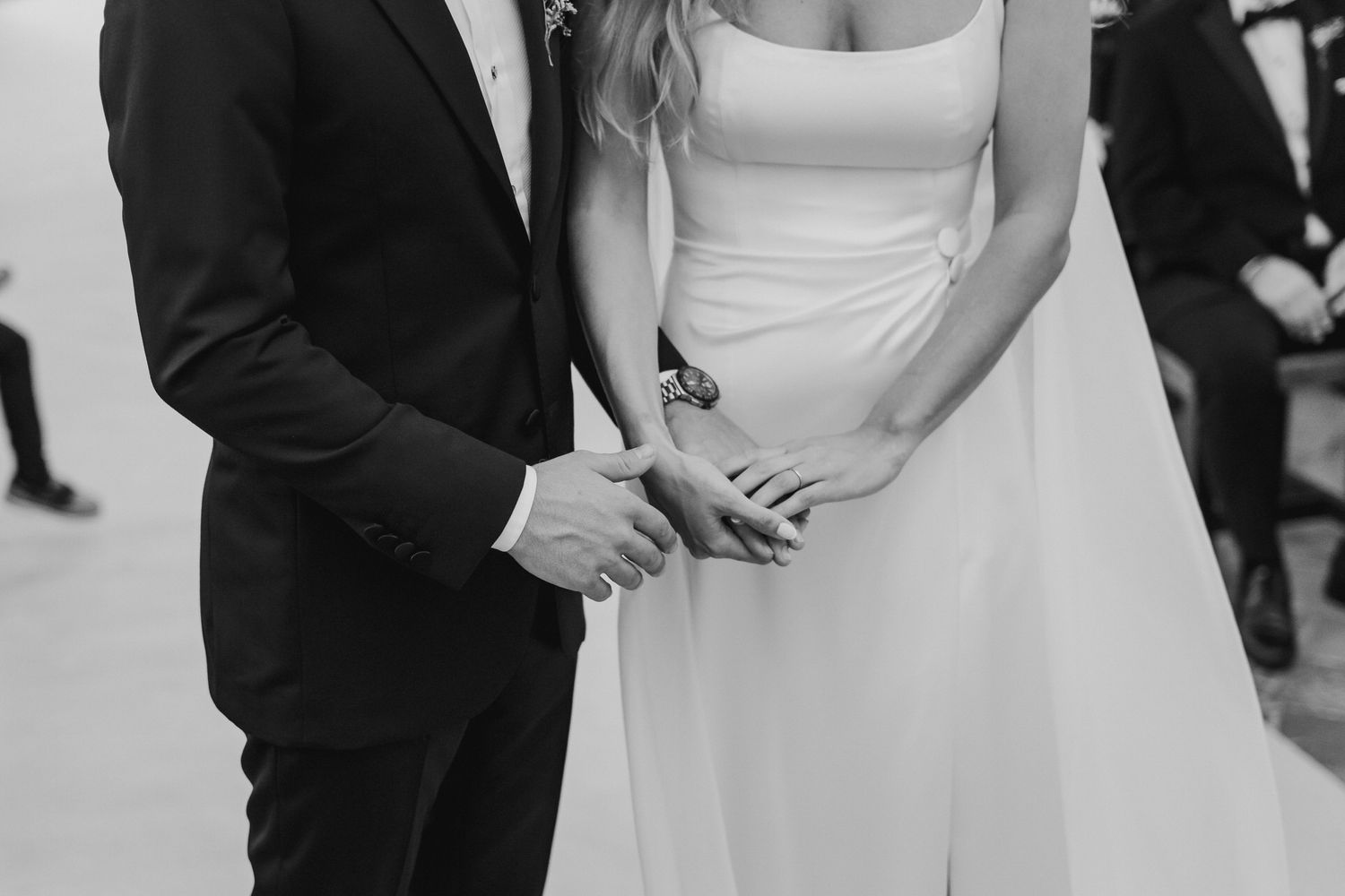 Black and white close-up of bride and groom holding hands during outdoor wedding ceremony.