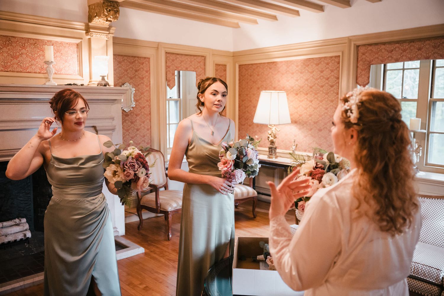 Bride laughing with two bridesmaids in sage green dresses during wedding day preparations at Searles Castle.