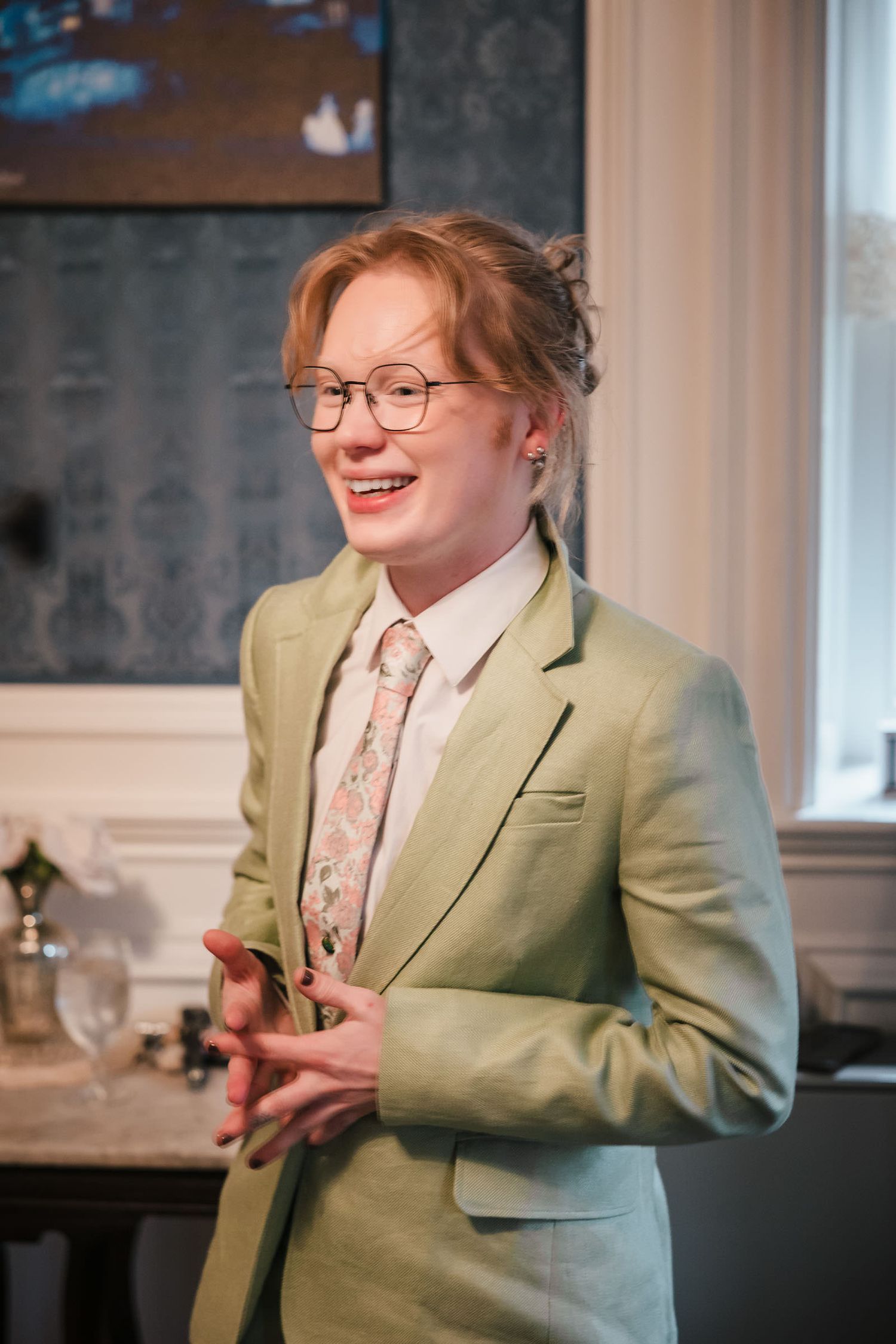 Bridesmaid in a sage green suit and floral tie, smiling during wedding day preparations