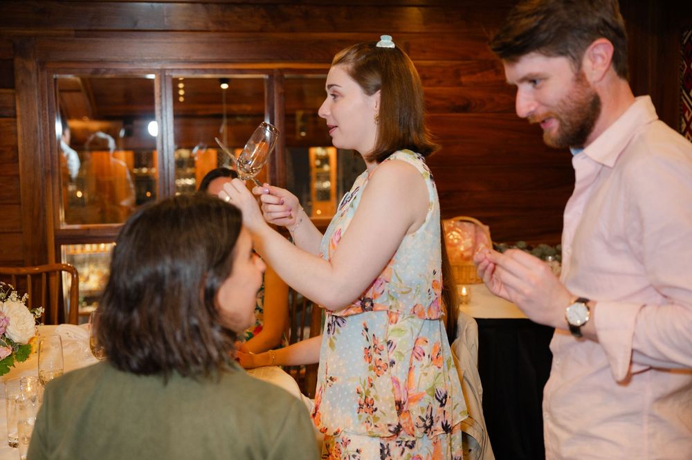 Woman in floral dress holds trophy while interacting with guests at an indoor dinner party event.