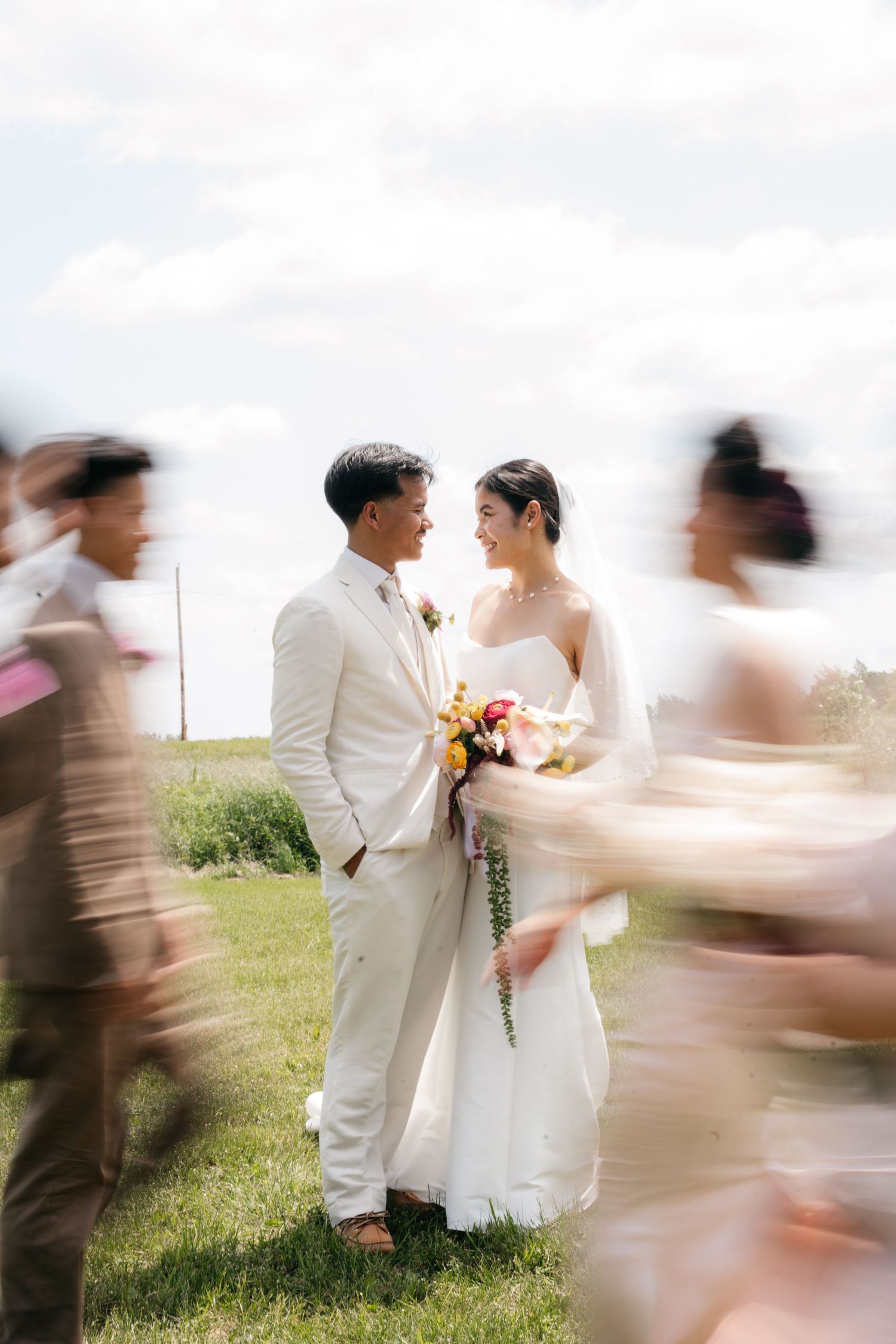 Bride and groom share a romantic moment outdoors as wedding guests blur around them in motion.