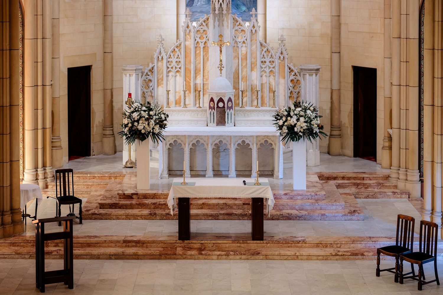 Interior view of a Gothic church sanctuary with vaulted ceilings, wooden pews, and an ornate altar decorated with flowers.