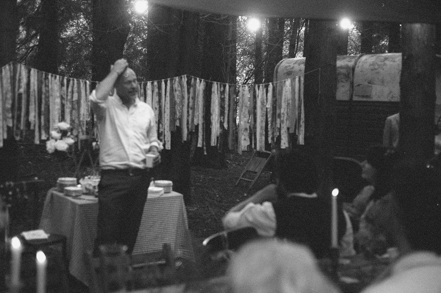 Black and white outdoor dinner party with man standing at table, string lights and fabric banners in background.