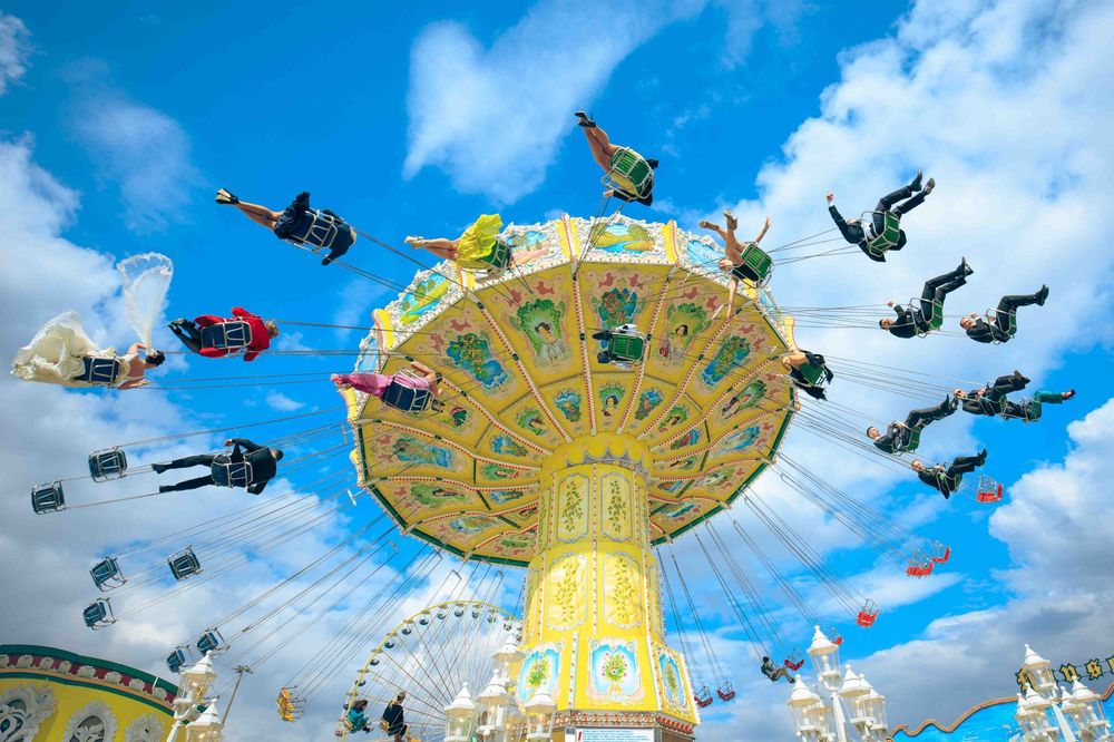 Colorful carnival swing ride with riders soaring high against a bright blue sky at an amusement park.